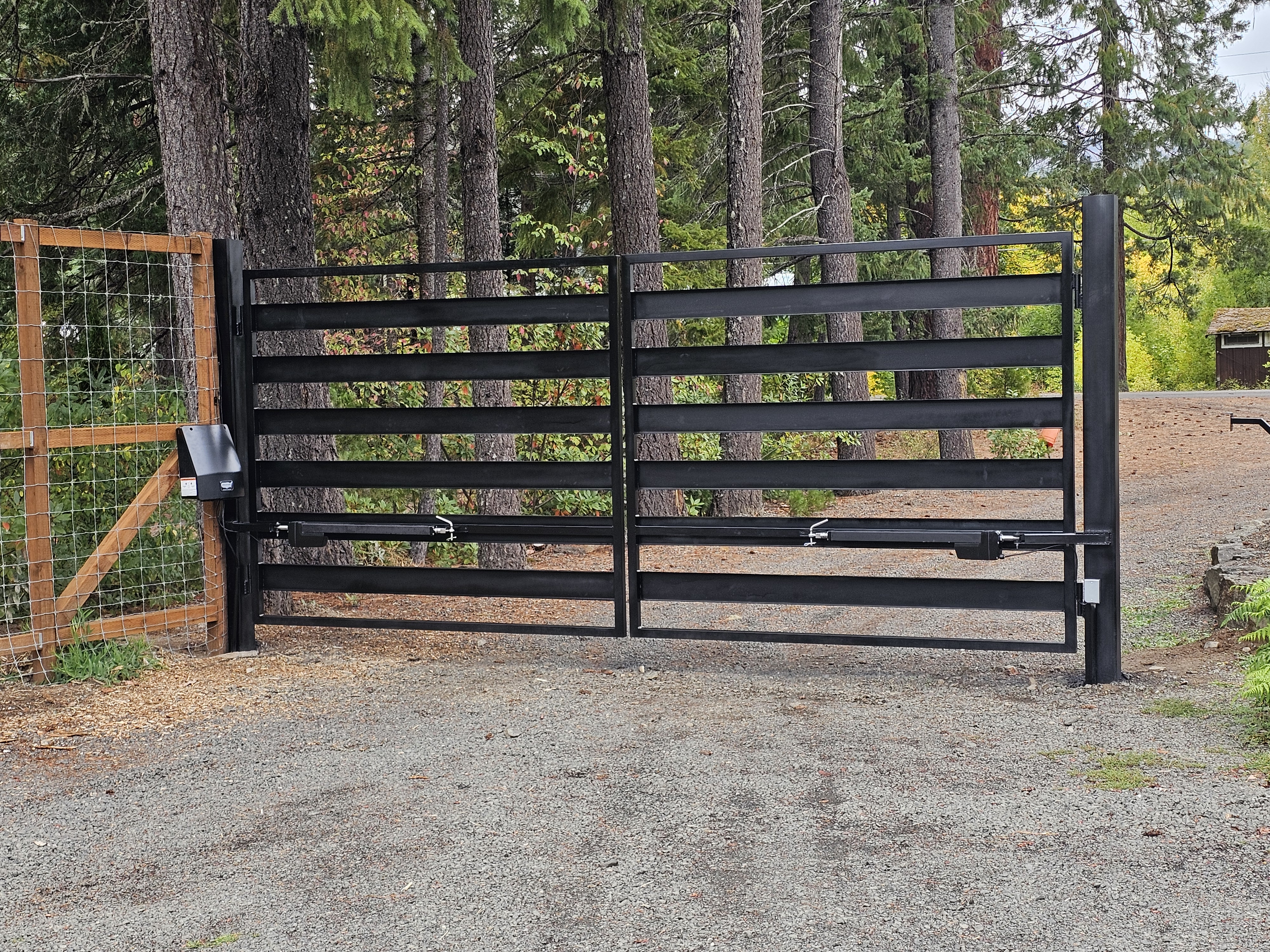 Automated black steel gate with wood fence and forest background